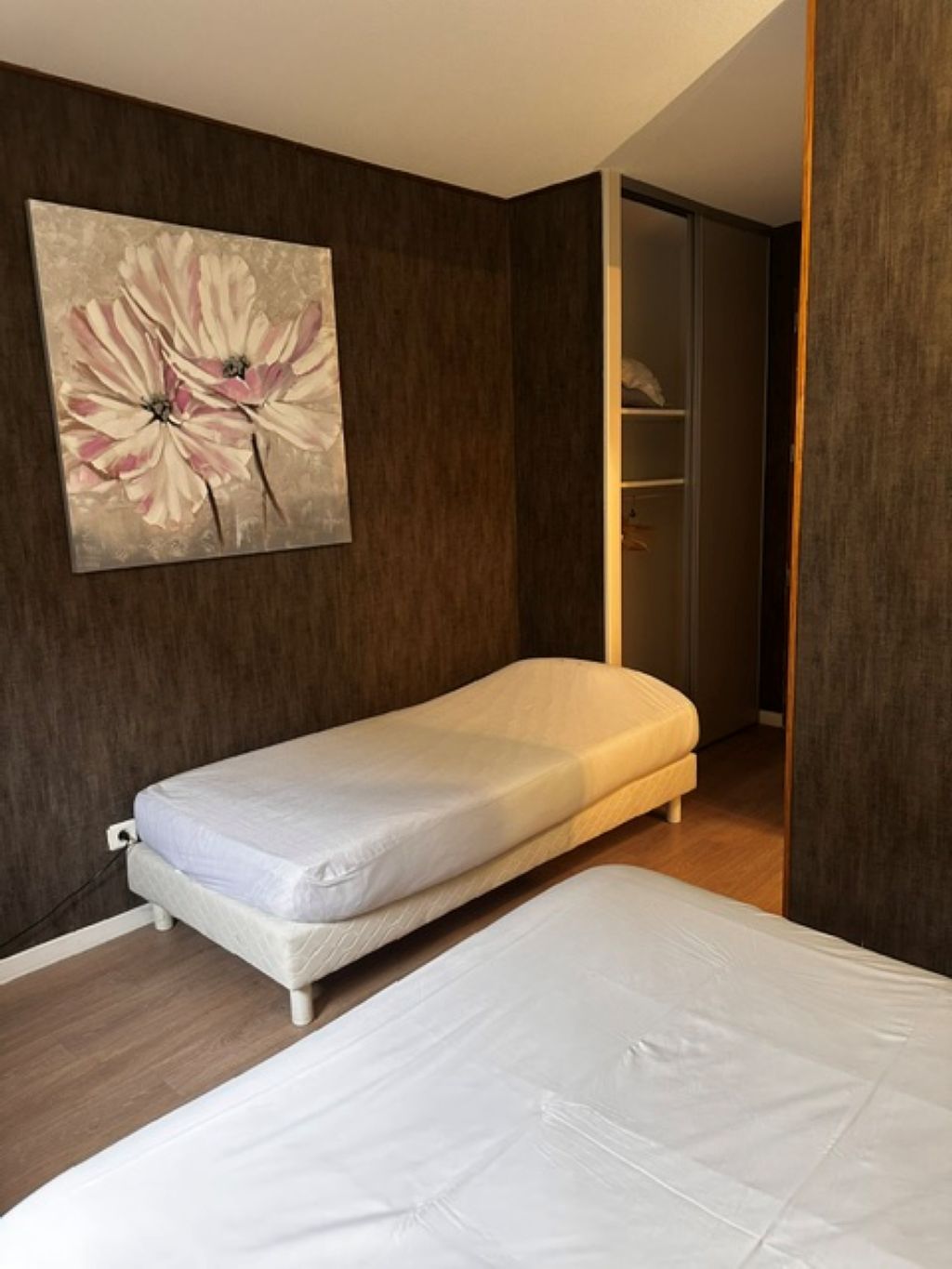 A bedroom with a single bed, a nightstand, a wall-mounted artwork, and a wardrobe.