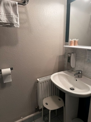 A bathroom with a white sink, a toilet, a radiator, a towel rack, and a small stool.