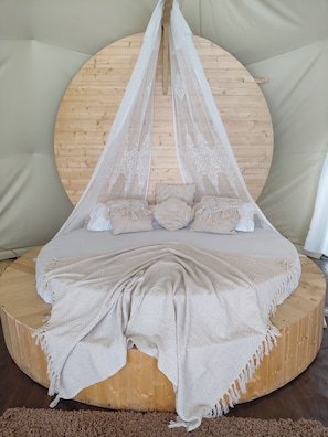 Una cama redonda de madera con dosel, una colcha color beige y almohadas.