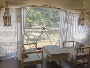 Una carpa con una mesa y dos sillas, vistas al exterior y decoraciones de macramé colgadas.