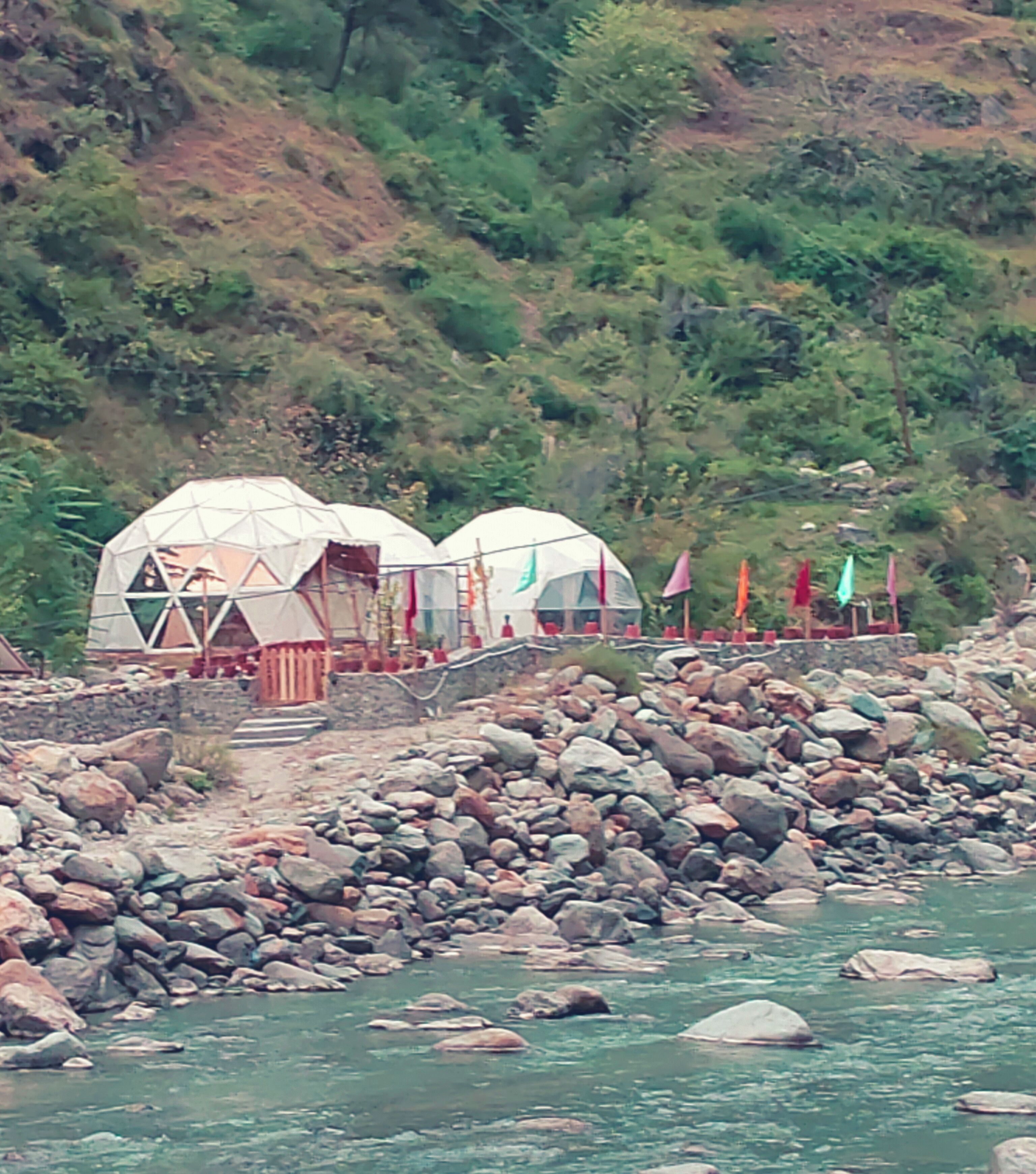 A riverbank with several dome-shaped structures, possibly tents, and a stone wall.