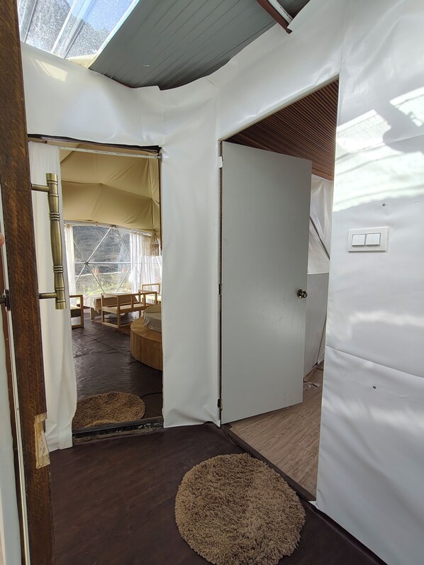 A room with a wooden floor, a white door, and a view of an outdoor area with a tent and furniture.
