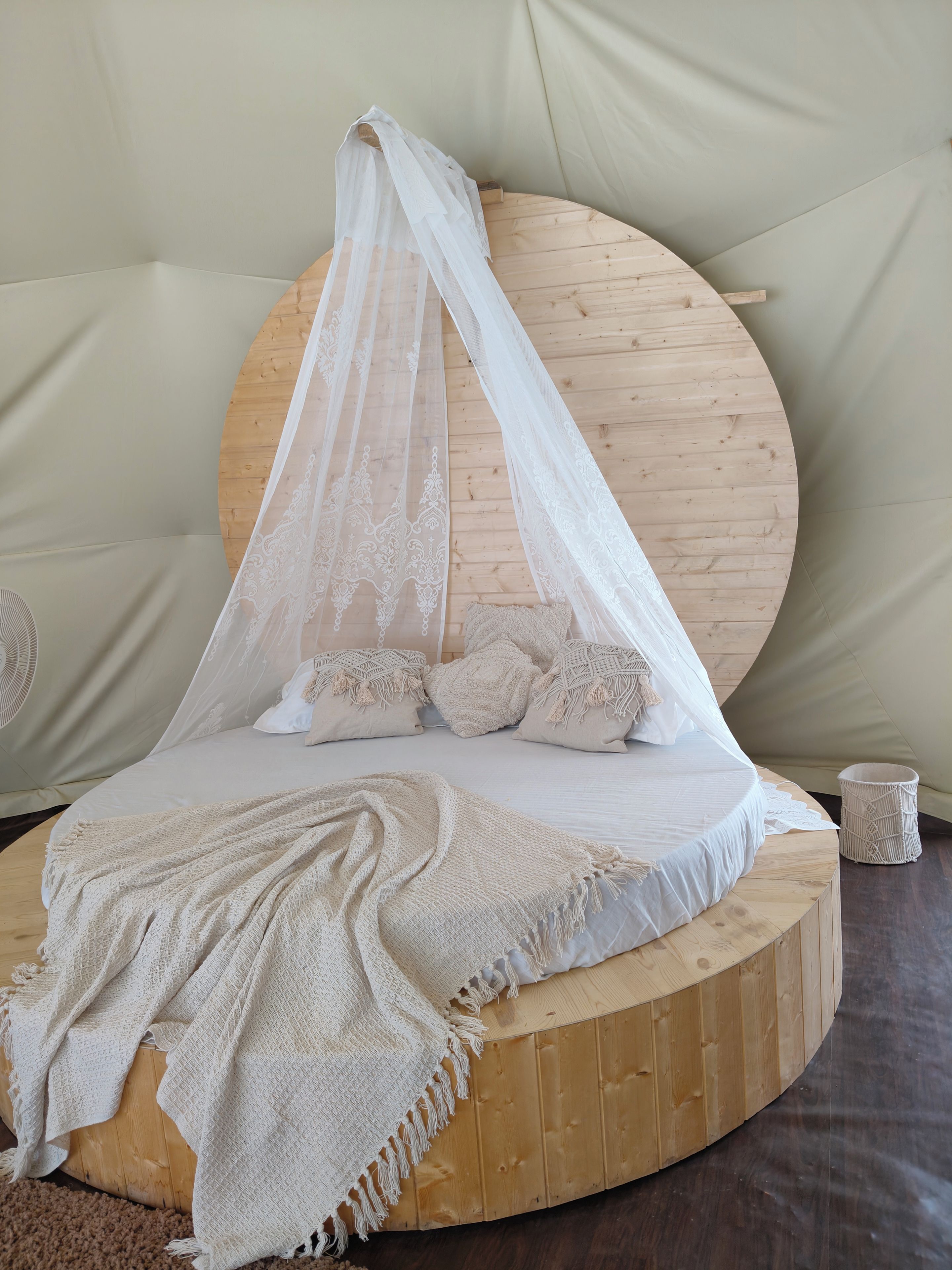 A round wooden bed with a canopy, multiple pillows, a blanket, and a woven basket.