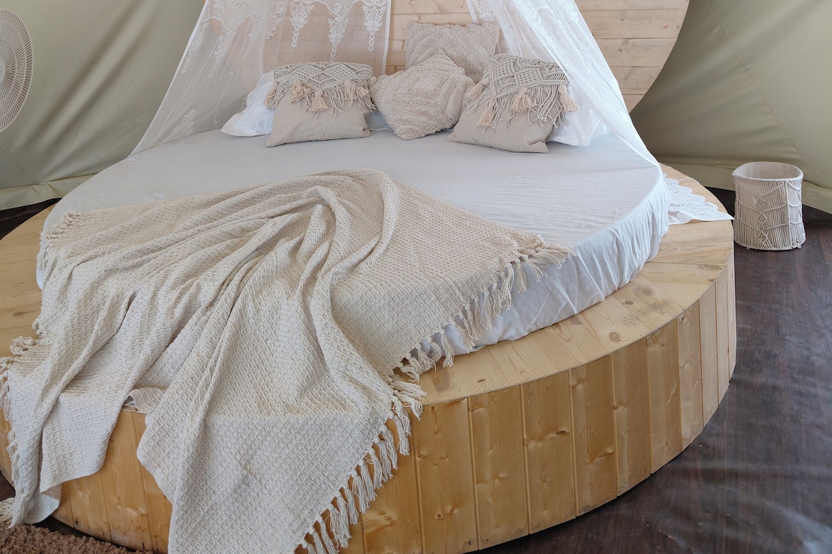 Una cama redonda de madera con dosel, varias almohadas, una manta y una cesta tejida.