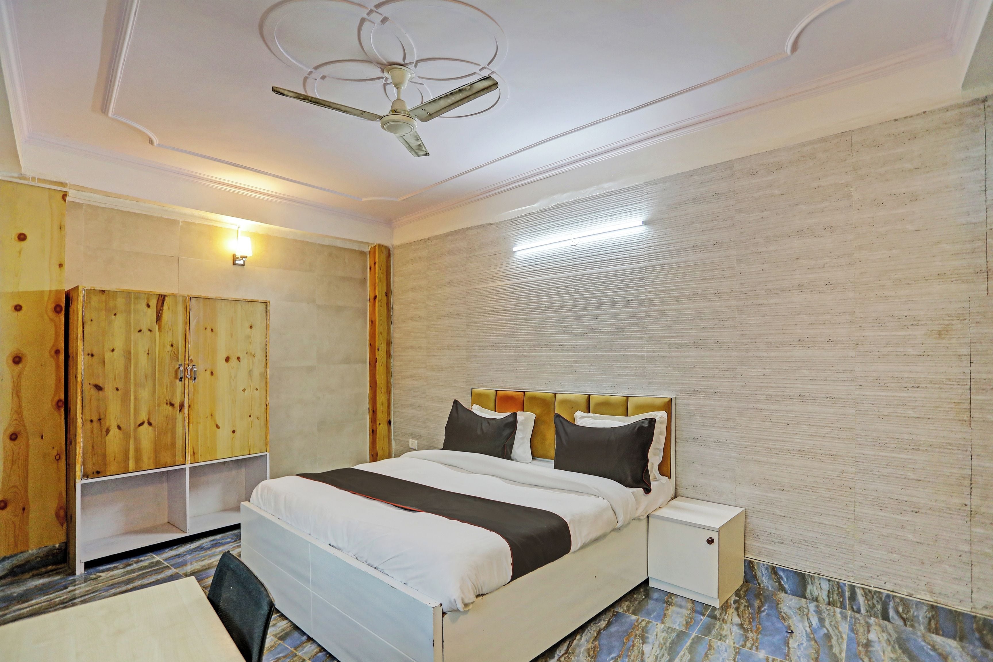 A hotel room with a bed, bedside table, wardrobe, ceiling fan, and a light fixture.