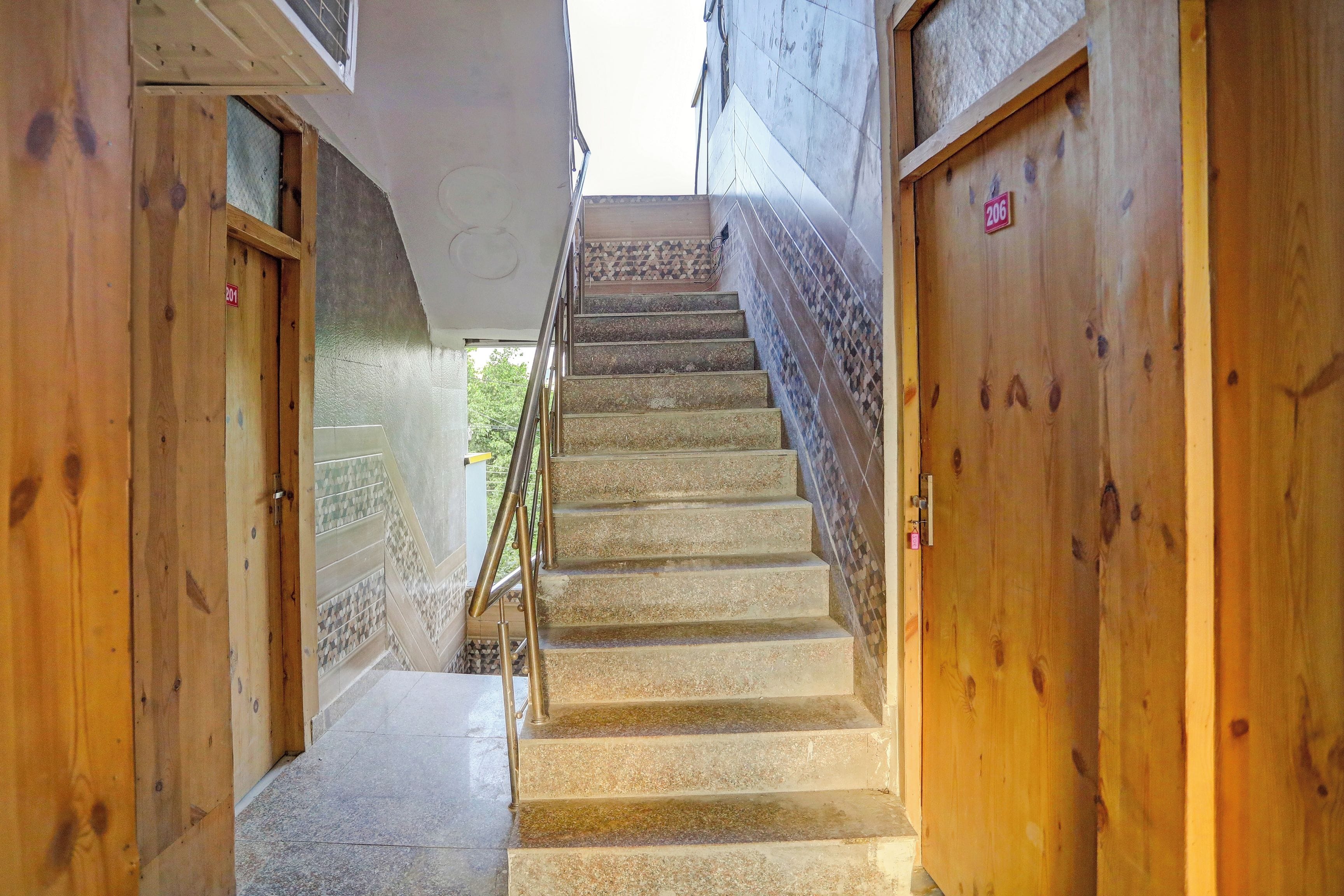 A narrow stairway leading to a wooden door with a number sign, flanked by wooden walls and a tiled floor.