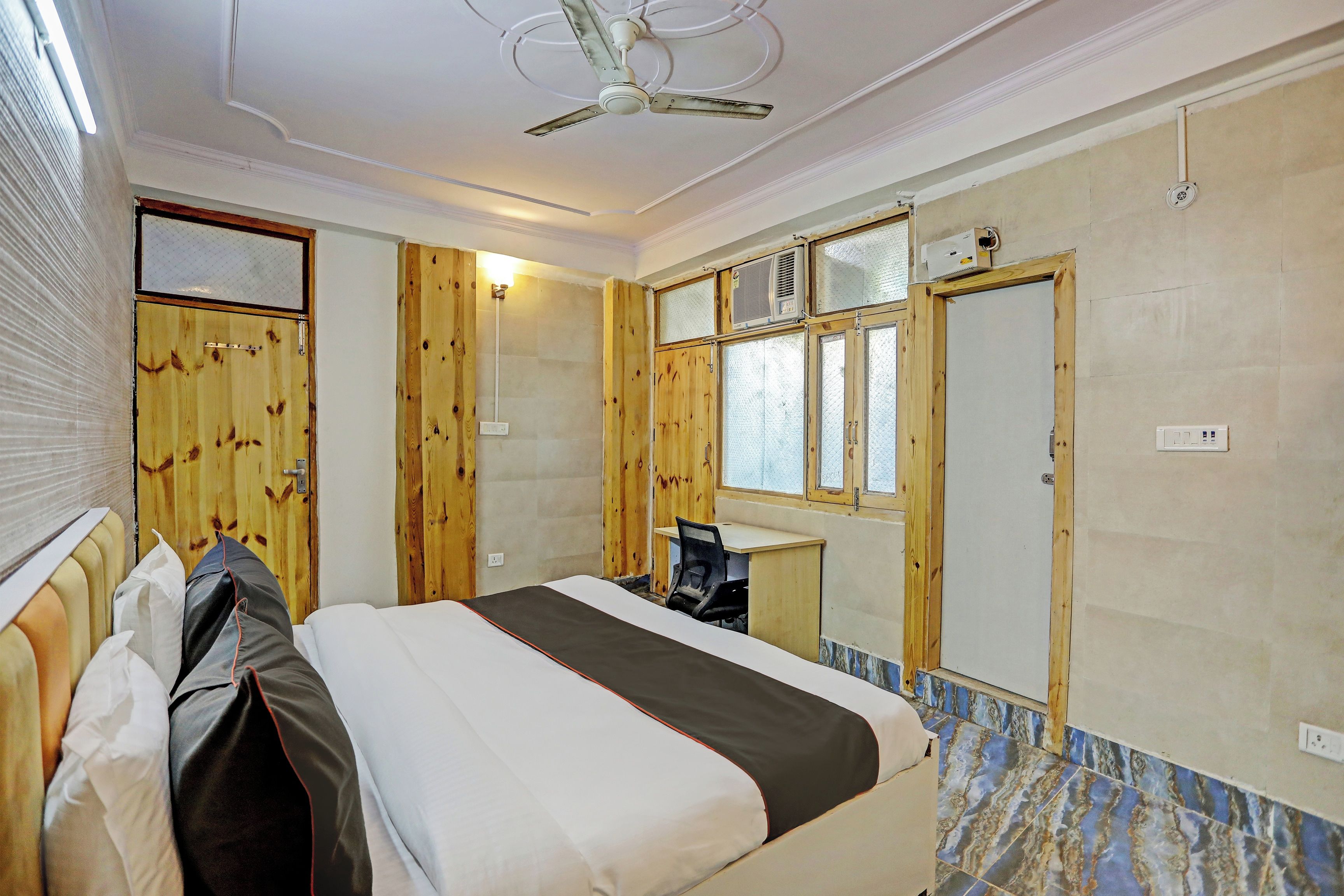 A hotel room with a bed, a desk, a ceiling fan, and a window with blinds.
