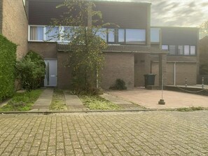A building with a brick facade, a small garden area with a pathway, and a trash bin. - Sleedoornstraat 15 (Cadzand-Bad)