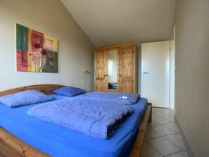 A bedroom with a large bed, wooden wardrobe, and a painting on the wall. - Sleedoornstraat 15 (Cadzand-Bad)
