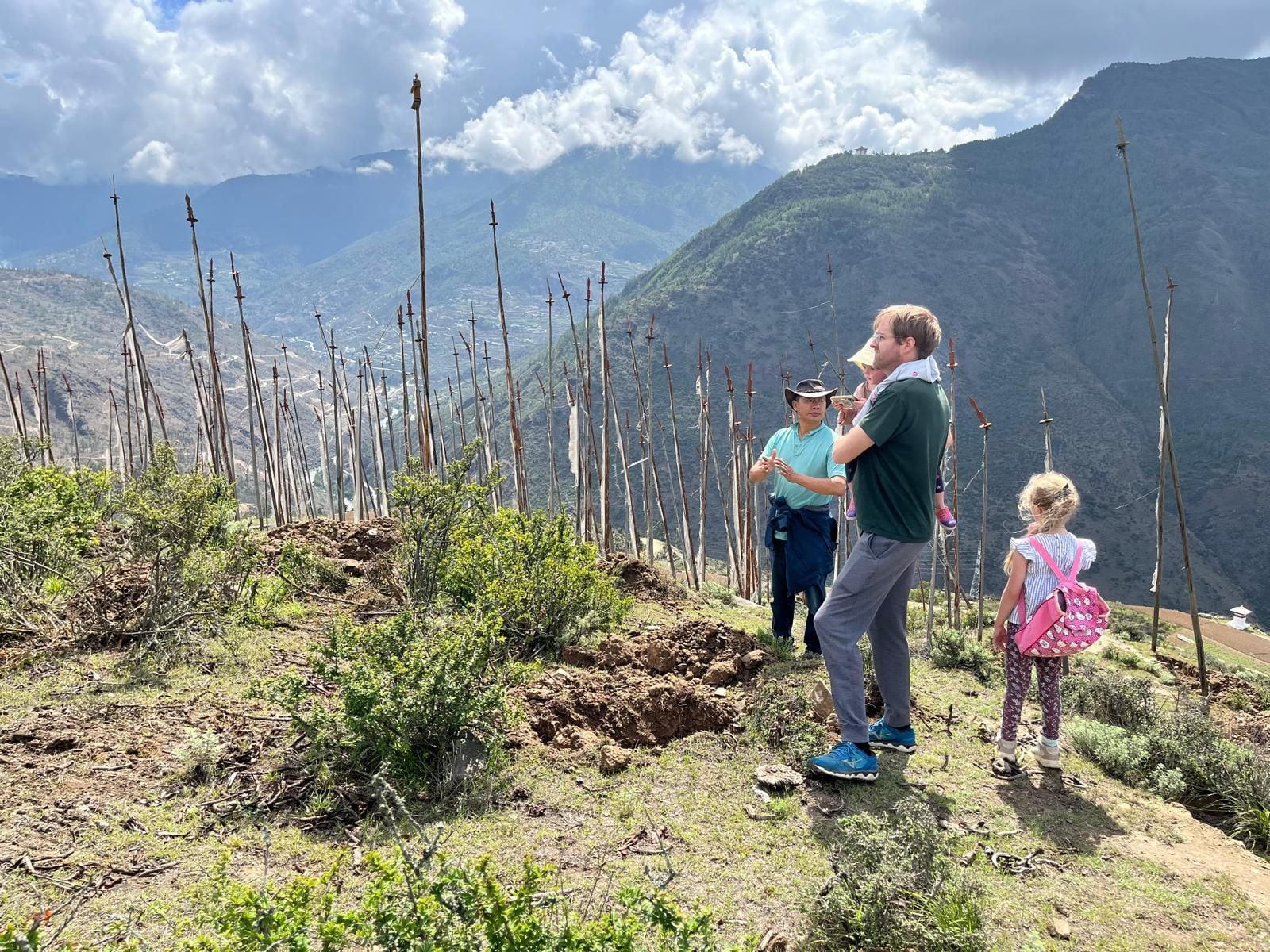 A group of people on a mountain trail with a view of a valley and mountains in the background.