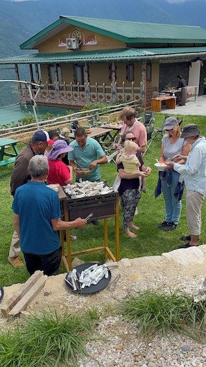 A group of people gathered around a grill outdoors with a building in the background. - The Happiness Farm (Paro)
