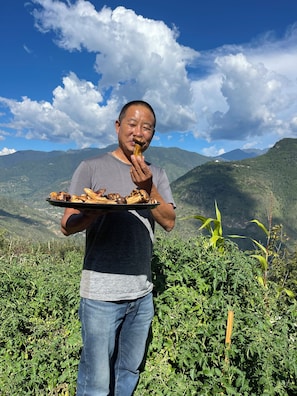 A person holding a plate with food, standing in a natural setting with mountains in the background. - The Happiness Farm (Paro)