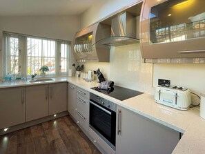 A modern kitchen with a built-in oven, a toaster, and a window with a view of trees. - 2 bedroom accommodation in Whitby (Whitby)