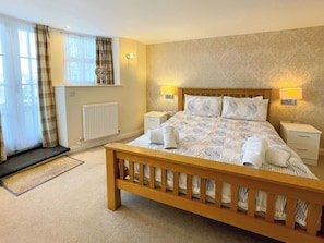A hotel bedroom with a wooden bed, two bedside tables, a radiator, and a window with curtains. - 2 bedroom accommodation in Whitby (Whitby)