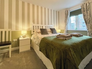 A hotel room with a striped wall, a single bed with a green bedspread, a bedside table with a lamp, a chair, and a window with curtains. - 2 bedroom accommodation in Whitby (Whitby)