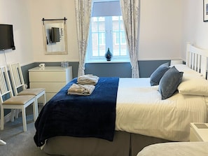 Habitació d'hotel amb un llit, escriptori, cadira, televisió i finestra amb cortines.