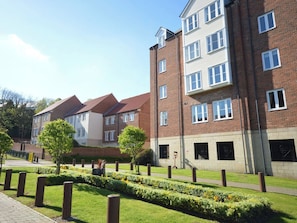 A residential building with multiple floors, brick exterior, and a well-maintained garden with hedges and flower beds. - 2 bedroom accommodation in Whitby (Whitby)