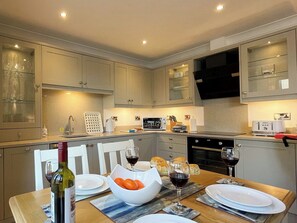 A modern kitchen with built-in appliances, a dining table set for a meal, and a wine bottle. - 2 bedroom accommodation in Whitby (Whitby)