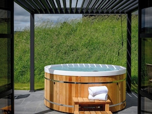 A hot tub with a wooden exterior, a bench, and a towel, set against a backdrop of tall grass and a clear sky. - 2 bedroom accommodation in Ravensworth (Ravensworth)