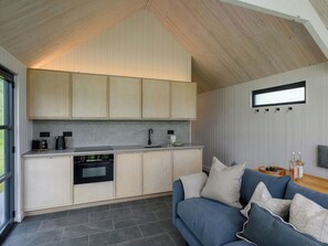 A modern kitchen with wooden cabinets, a built-in oven, and a dining area with a blue sofa and cushions. - 2 bedroom accommodation in Ravensworth (Ravensworth)