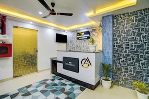 A reception area with a marble wall, a reception desk, a television, and a ceiling fan. - Townhouse GRAND ADDRESS HOTEL  (Ghaziabad)