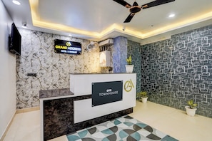 A hotel reception area with a marble wall, a ceiling fan, and a reception desk. - Townhouse GRAND ADDRESS HOTEL  (Ghaziabad)