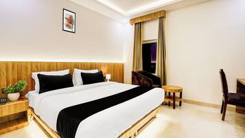 Ein Hotelzimmer mit einem großen Bett, einem Schreibtisch, einem Sessel, einem kleinen Tisch, einer Topfpflanze und einem Deckenventilator.
