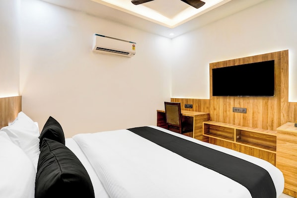A hotel room with a bed, a desk, a chair, a flat-screen TV mounted on the wall, and an air conditioning unit. - Townhouse GRAND ADDRESS HOTEL  (Ghaziabad)