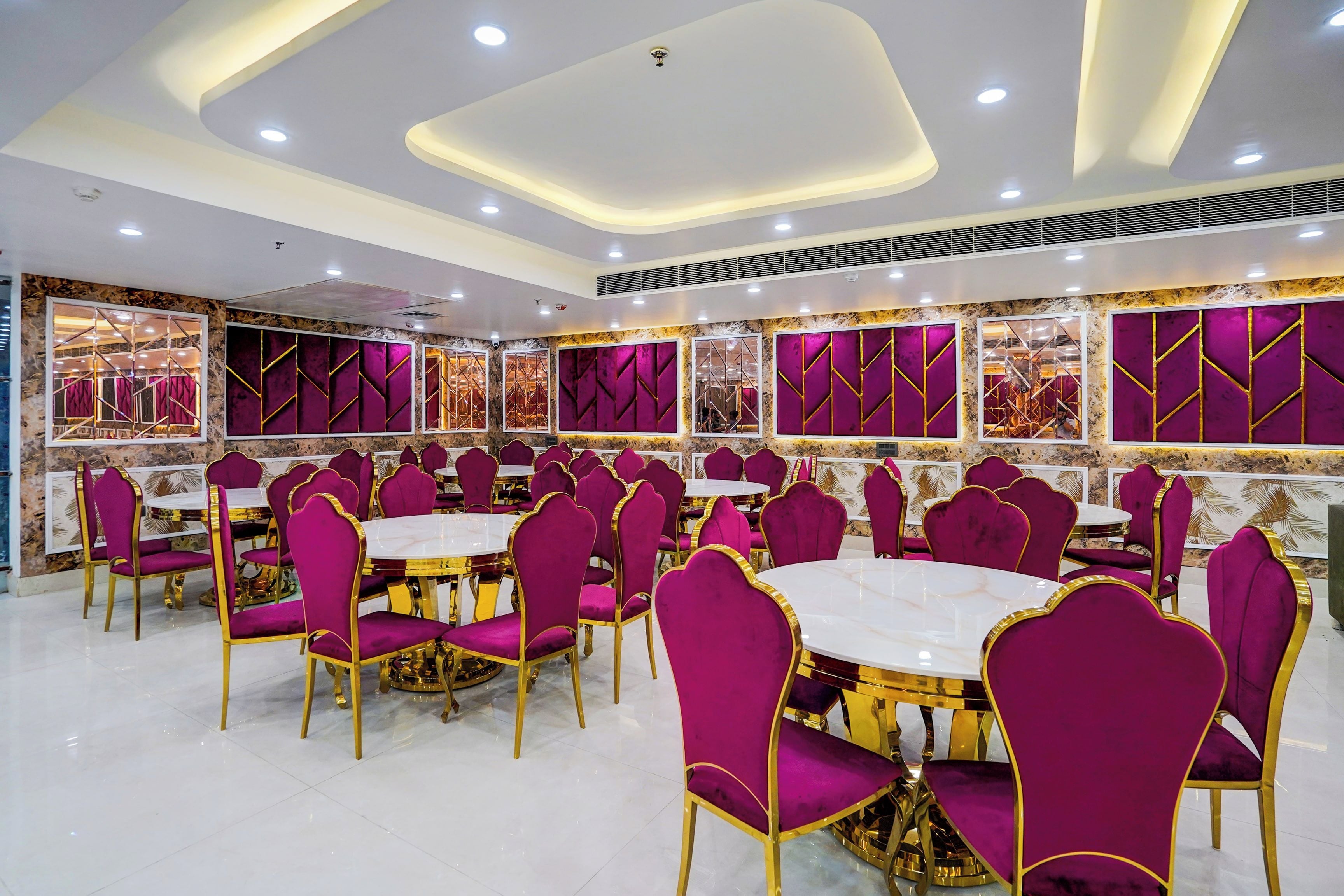 A spacious dining area with round tables and chairs, marble walls, and a modern ceiling design.