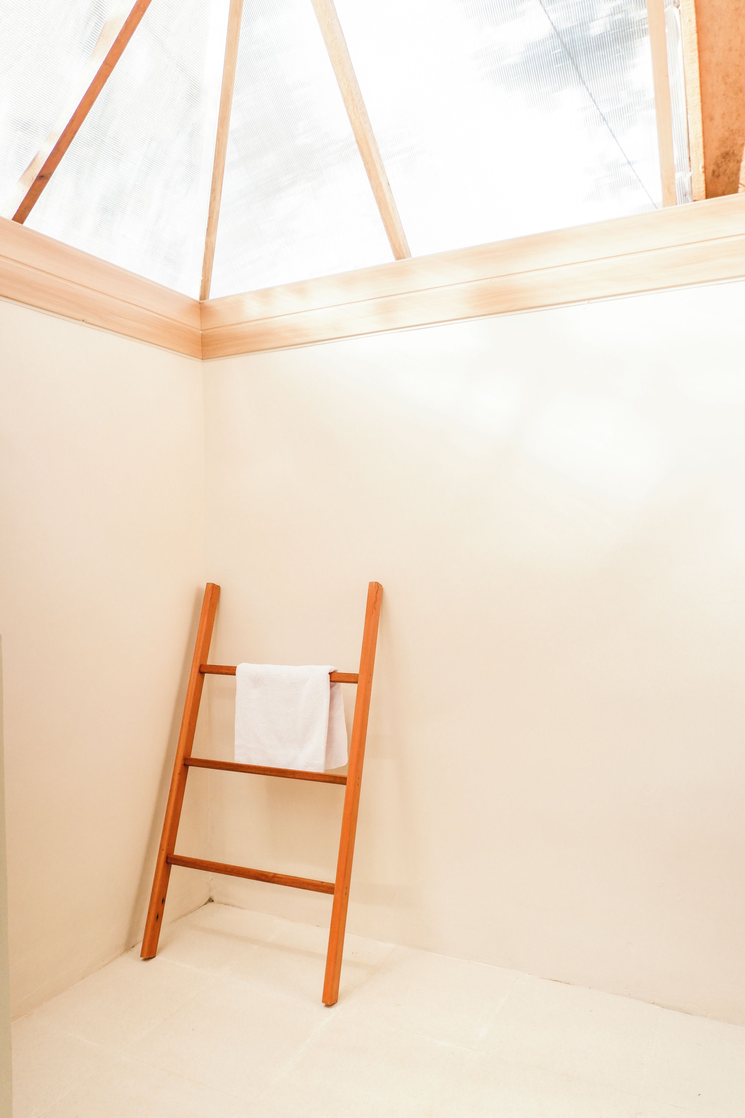 A corner of a room with a wooden ladder leaning against the wall and a white towel hanging on it.