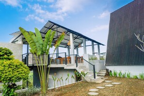 A modern building with a covered outdoor seating area, a staircase, and a garden with various plants.
