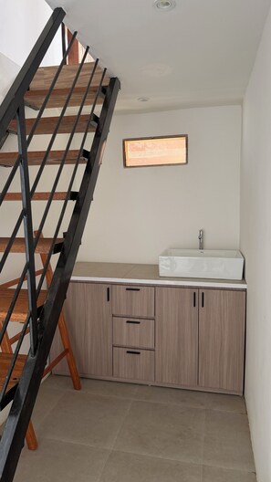 A staircase with wooden steps and black metal railings leading to a kitchen area with a sink and cabinets.