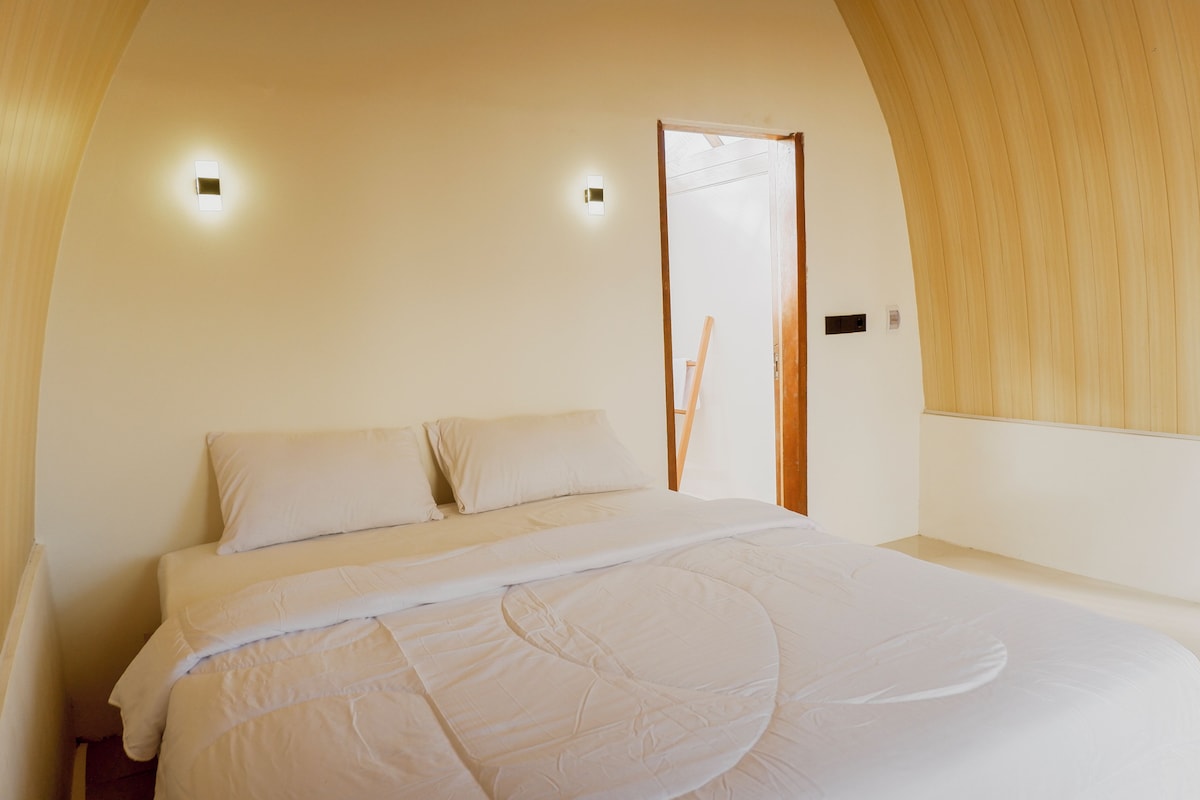 A bedroom with a bed, pillows, a wooden door, and a light fixture.
