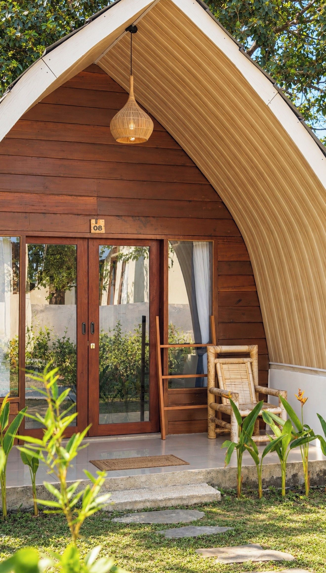 A wooden cabin with a sloped roof, a glass door entrance, a wicker chair, and a hanging light fixture.