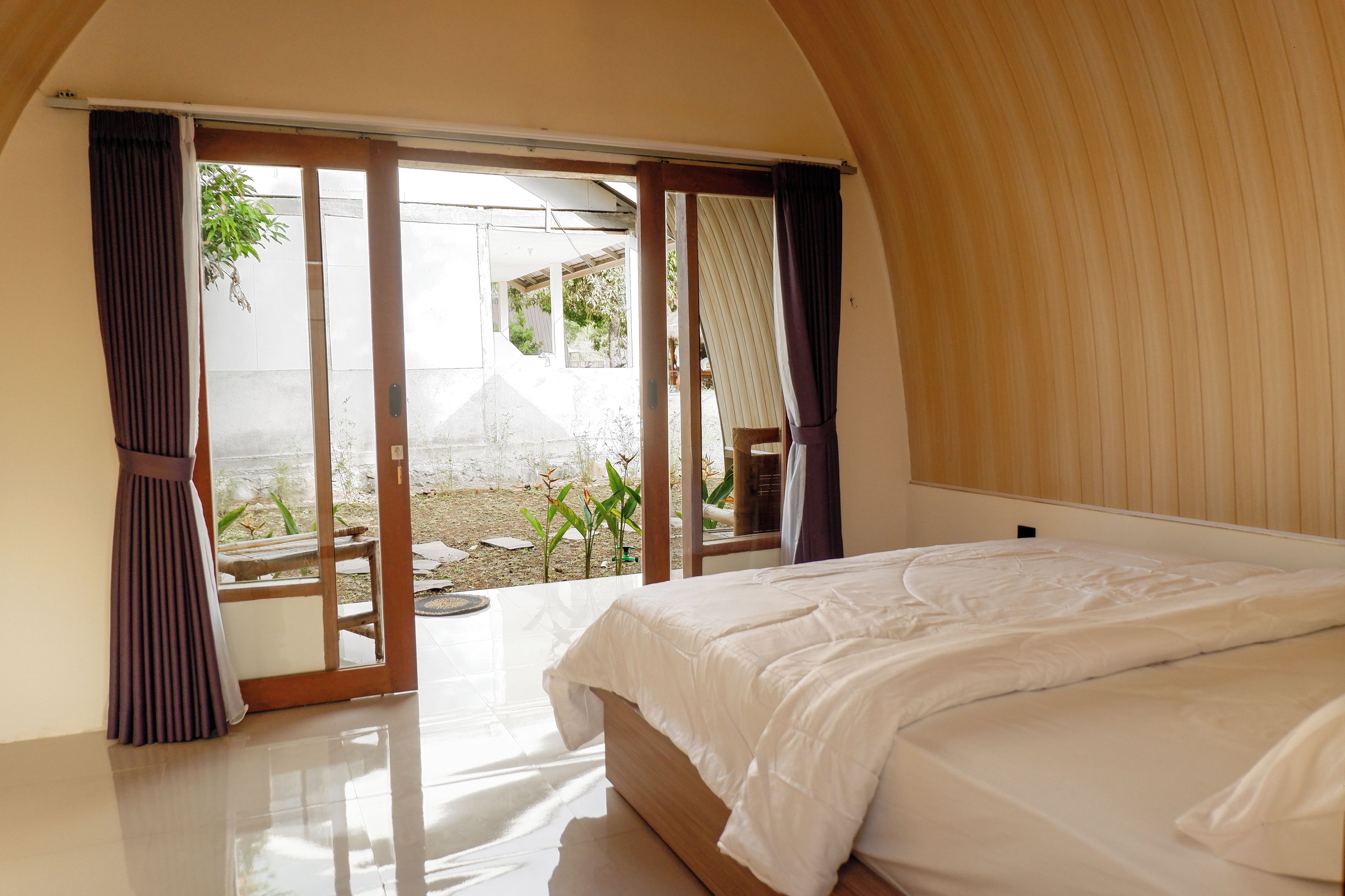 Un dormitorio con una cama grande, un ventanal corredero que da a un espacio exterior y techo de madera.
