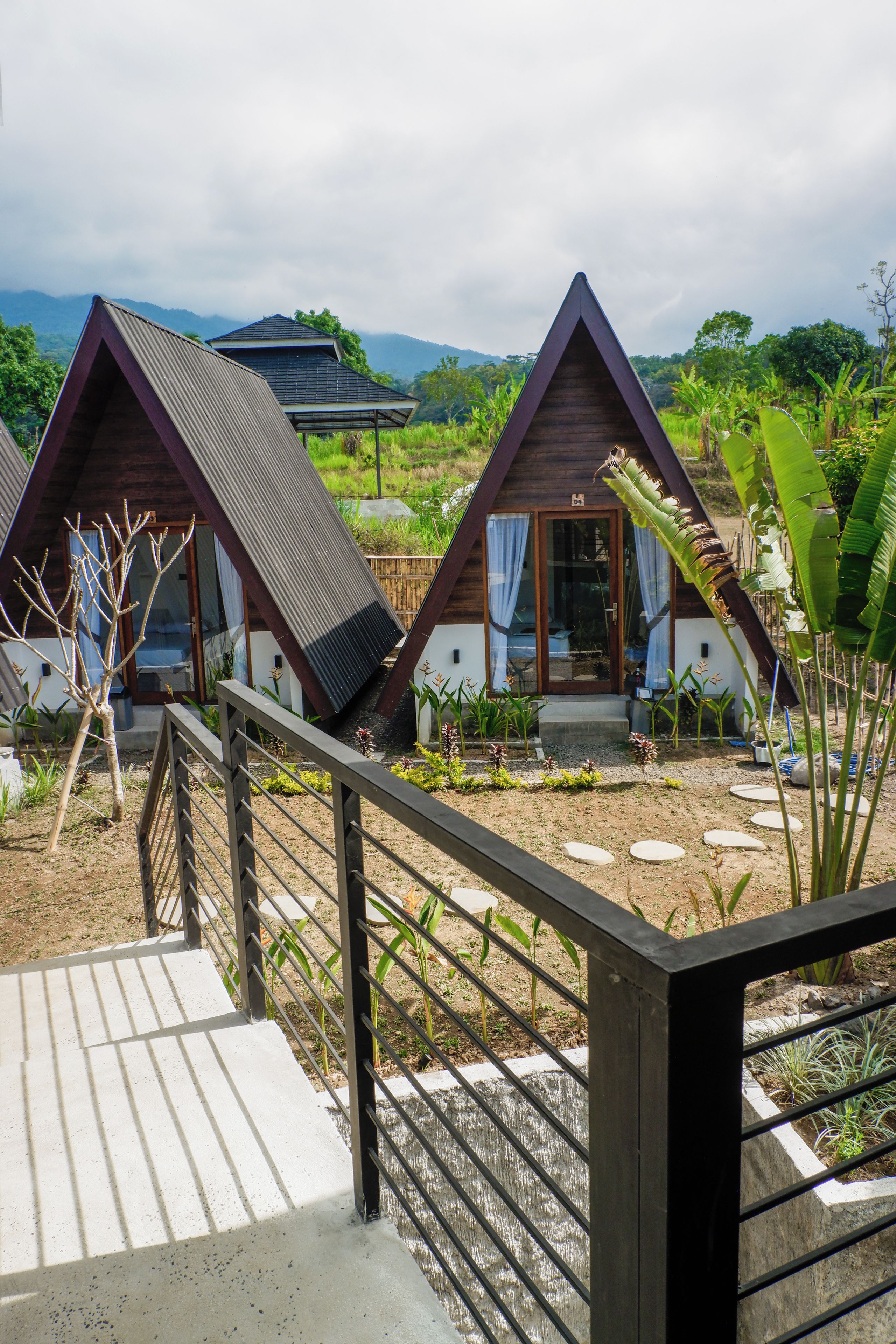 A bungalow-style accommodation with a sloped roof and a wooden facade, surrounded by lush greenery and a clear sky.