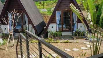 Ein bungalowähnliches Gebäude mit geneigtem Dach und Holzfassade, umgeben von üppiger Vegetation und blauem Himmel.
