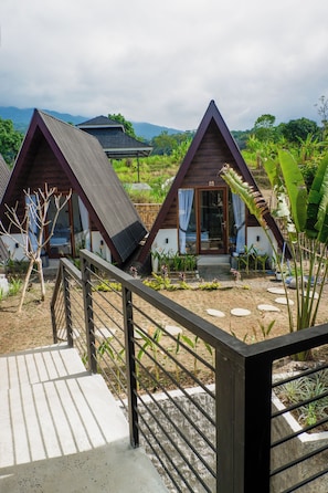 A bungalow-style accommodation with a sloped roof and a wooden facade, surrounded by lush greenery and a clear sky. - Windy Senaru (Kabupaten Lombok Utara)