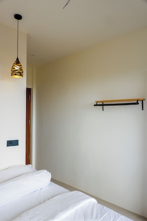A bedroom with a bed, a hanging light fixture, a wooden shelf, and a door.