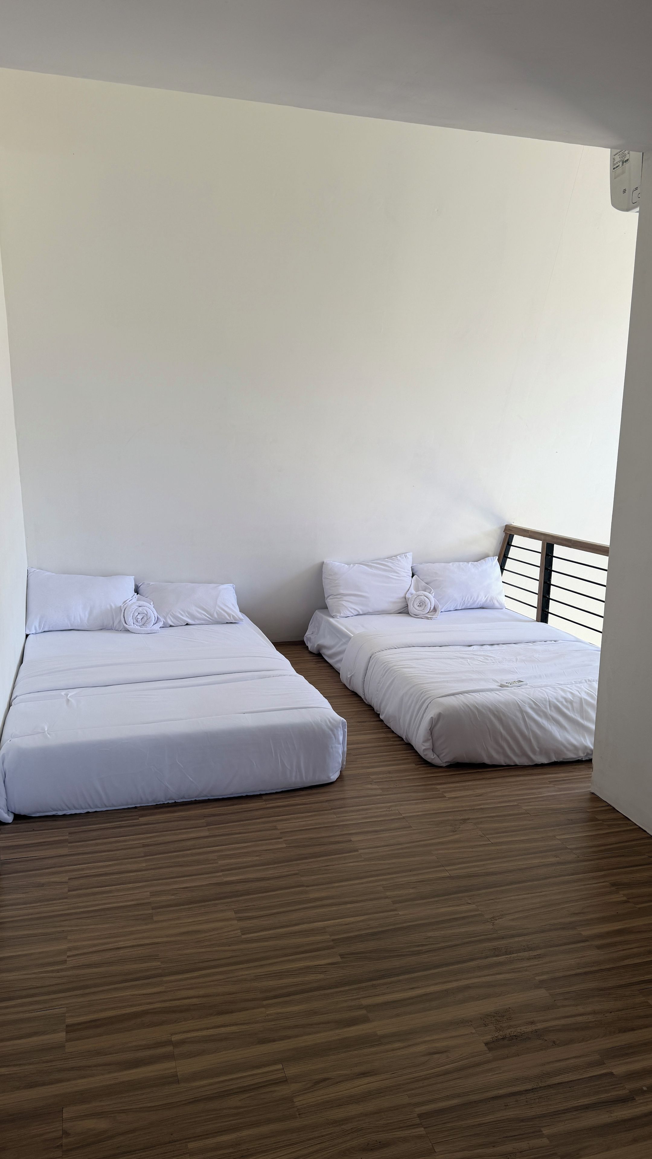 A room with two beds, wooden flooring, and white walls.
