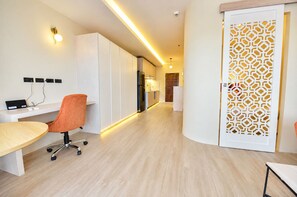 Une cuisine moderne équipée d’un réfrigérateur, un coin repas avec une table et une chaise orange, et une porte blanche décorative ornée d’un motif géométrique.