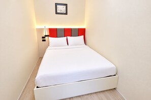 A neatly made bed in a hotel room with a headboard featuring red and gray panels, a wall-mounted light, and a framed picture above the bed. - Your Coastal Getaway Just Minutes From Jomtien Beach (Pattaya)