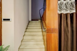 Eine Treppe mit Handlauf, einem Wandlüfter und einem gemusterten Vorhang.