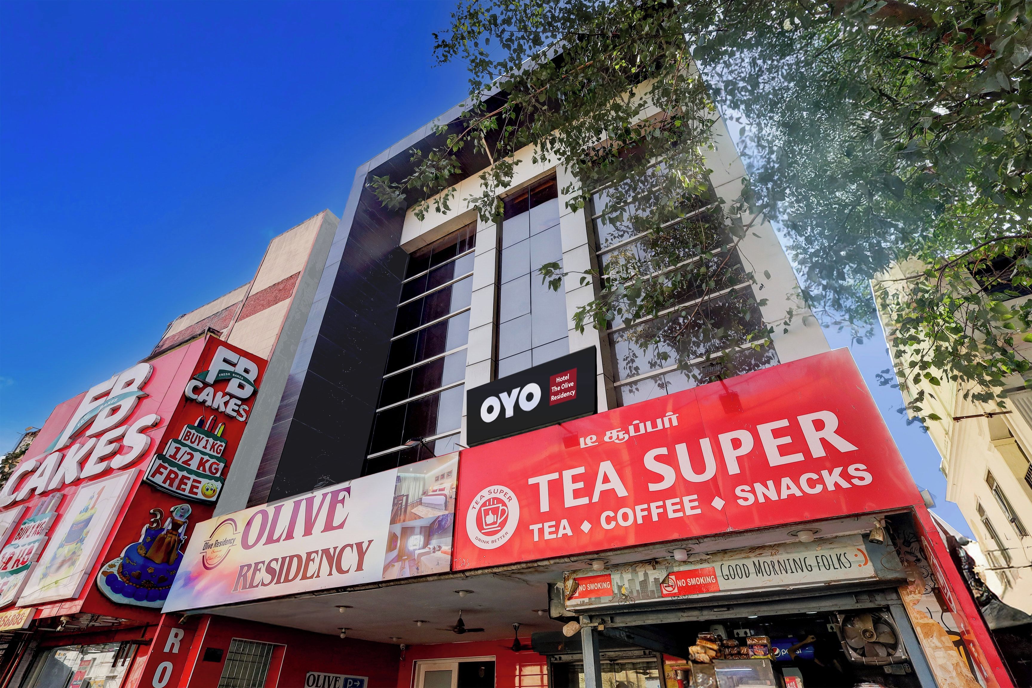 Un edificio de varios pisos con un letrero destacado que anuncia 'Olive Residency' y 'Tea Super', ofreciendo té, café y aperitivos.