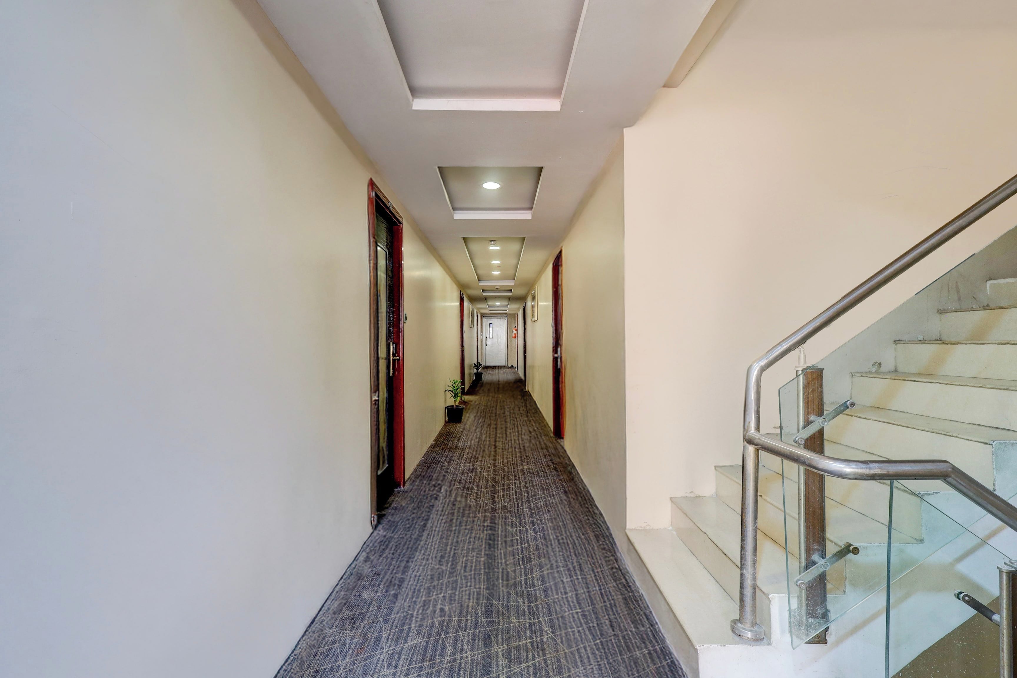 A hallway with a carpeted floor, doors, and a staircase with metal railings.