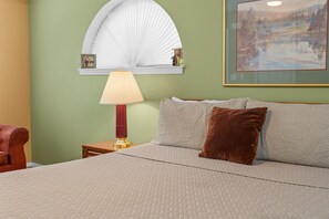 Une chambre à coucher comprenant un lit, une table de chevet, une lampe, un ventilateur fixé au mur et un tableau encadré.