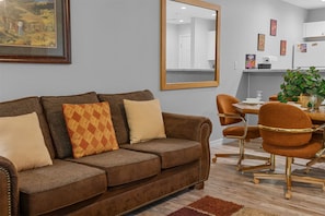 A living room with a brown sofa, a dining table with chairs, a mirror, and a framed picture on the wall. - Spring Creek Getaway (Branson)