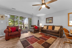 A spacious living room with a ceiling fan, a large window, and a view of the outdoors. - Spring Creek Getaway (Branson)
