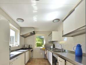 A kitchen with white cabinets, stainless steel appliances, a window, and a view of greenery outside. - Holiday Apartment With 2 Bedrooms (Renesse)