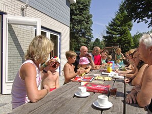 A group of people seated at an outdoor table with drinks and snacks, a brick building in the background, and a clear sky. - Holiday Apartment With 2 Bedrooms (Renesse)